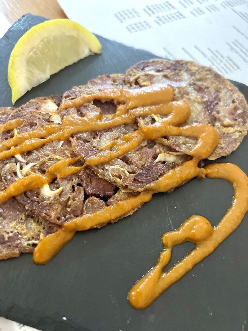 Una ración de tortitas de oreja crujiente con salsa brava.