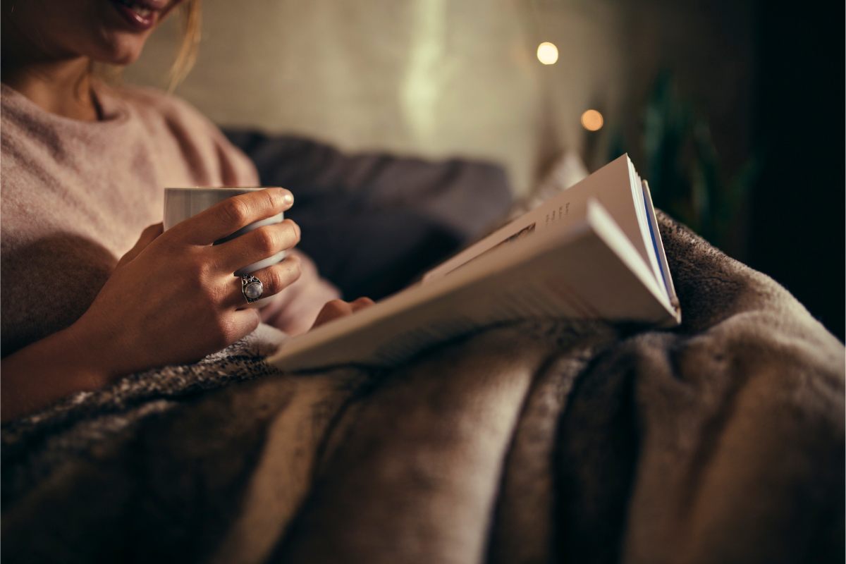 A woman reads a book in bed by the night.
