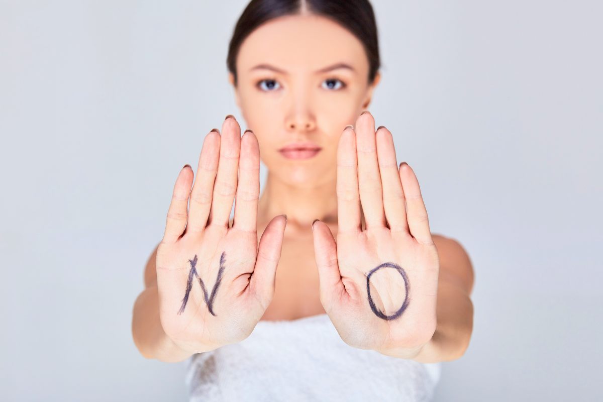 A young woman with her hands outstretched in a sign of setting boundaries with the letters NO written on her palms.