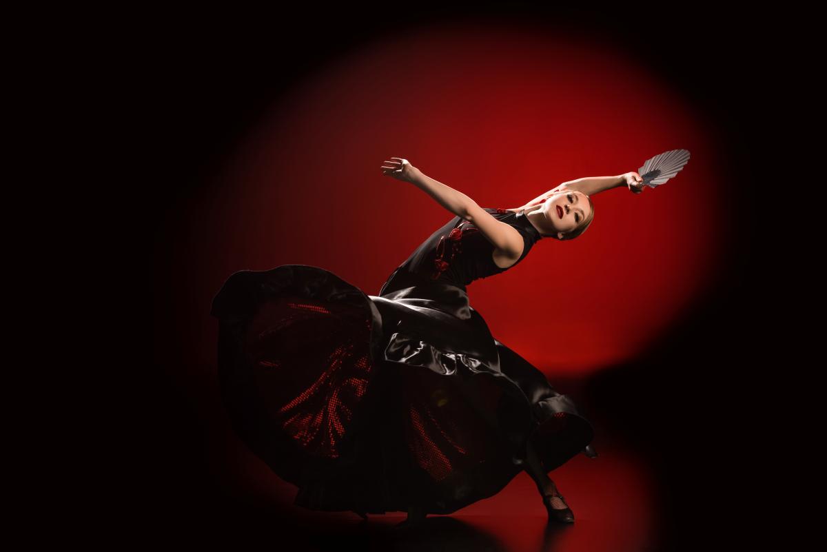A young woman dancing flamenco in a professional studio with a fan in her hand.