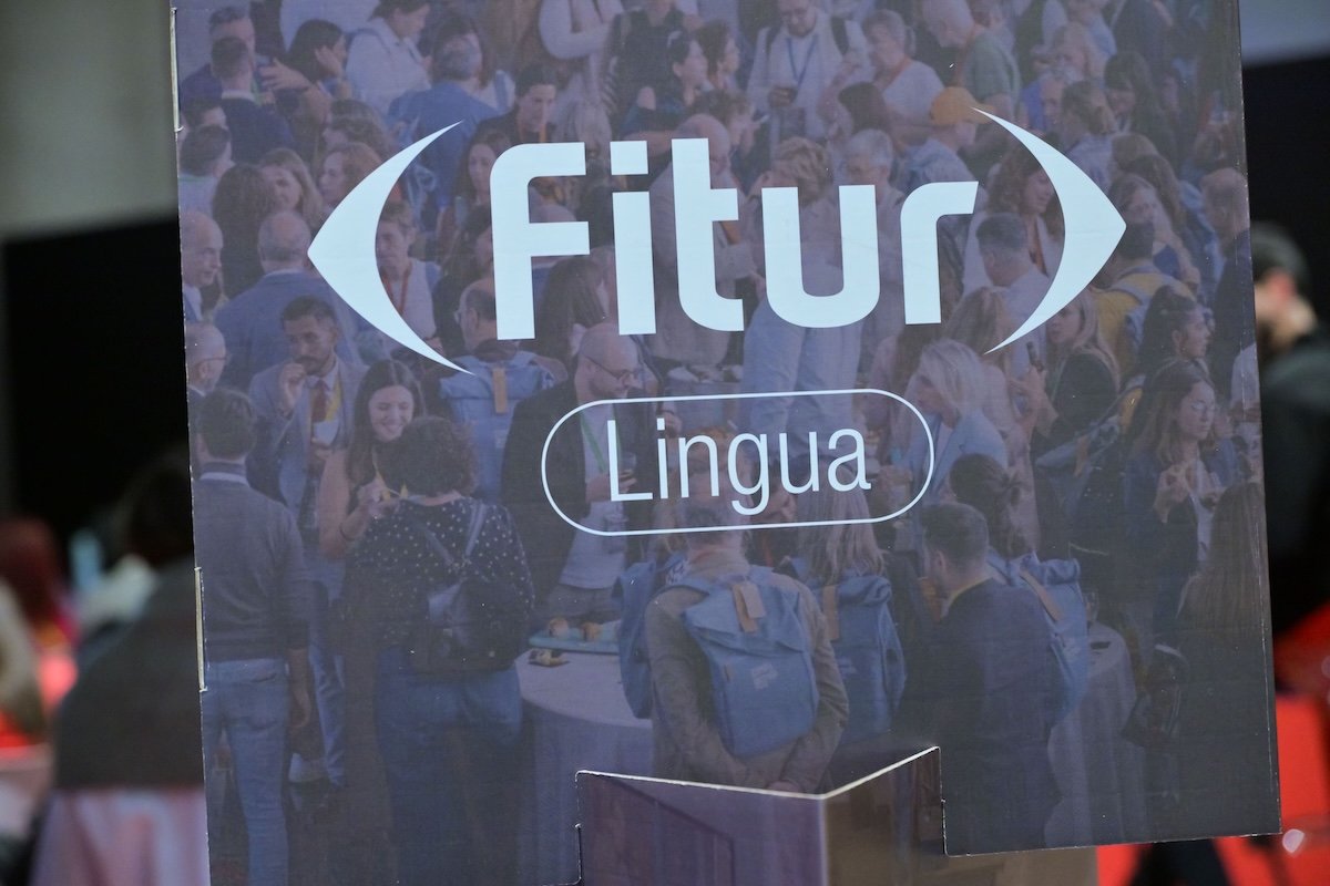 Close-up of a sign reading “Fitur Lingua” over a blurred background of a busy crowd at a trade fair.