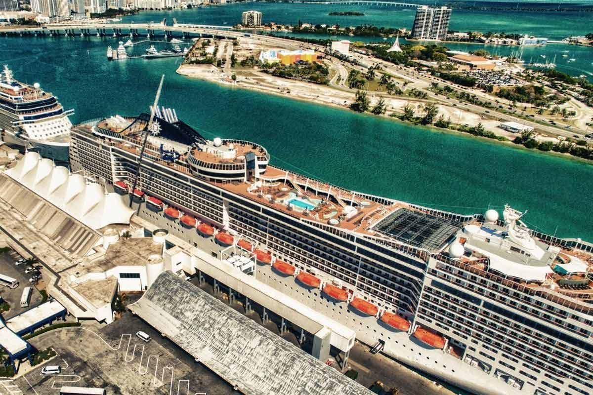 Aerial view of a large cruise ship docked at a port, with the city and bay in the background.