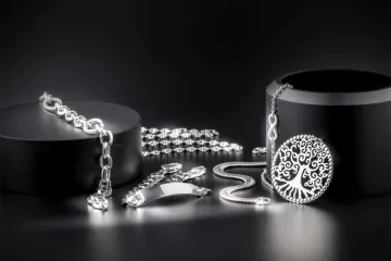 Tree-of-life pendant, chains, bracelets and an ID bracelet in silver arranged on black cylindrical display stands