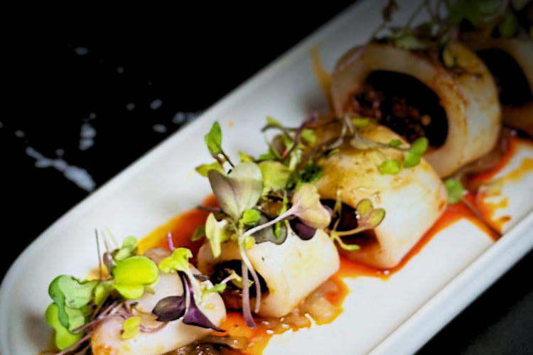 Gourmet dish with stuffed squid cut into rings, decorated with green sprouts and accompanied by a red sauce.