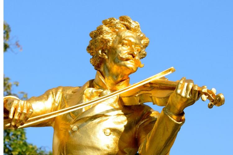 Close-up of the golden statue of Johann Strauss II playing the violin against a bright blue sky, showcasing intricate details of his face, hair, and violin.