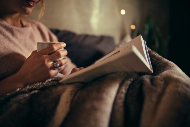 A woman reads a book in bed by the night.