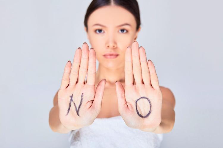 A young woman with her hands outstretched in a sign of setting boundaries with the letters NO written on her palms.