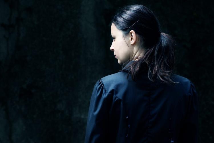 A woman dressed in black in a dark place, representing a psychological thriller, investigates.