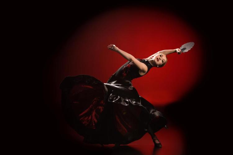 A young woman dancing flamenco in a professional studio with a fan in her hand.