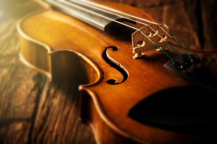 Close-up of a violin lying on a wooden surface, highlighting its warm, polished wood finish and intricate details like the f-holes and strings.