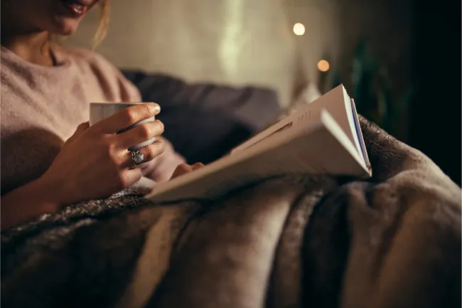 A woman reads a book in bed by the night.