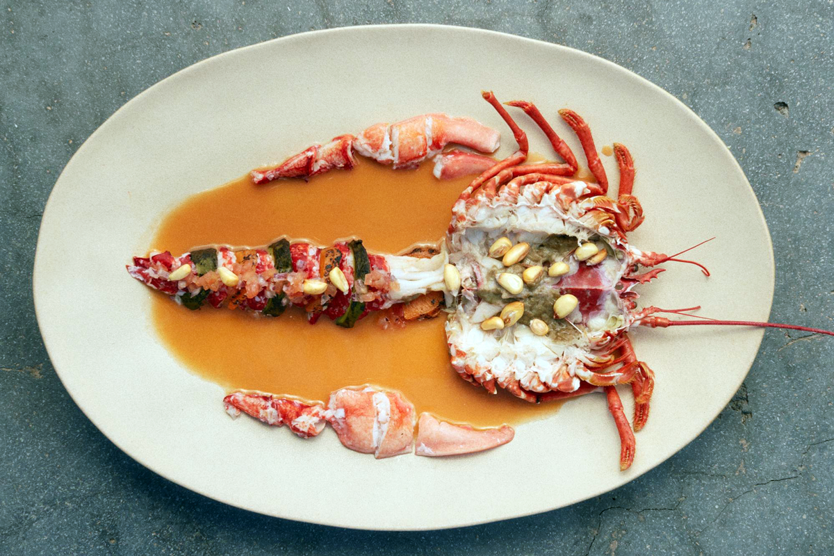Gourmet dish of lobster cut in half and presented on an oval tray. The lobster is decorated with peanuts and seaweed, and surrounded by sauce.